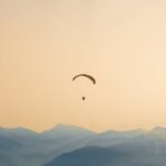 A paraglider soars gracefully over the misty, layered mountains at sunset, capturing serene adventure.